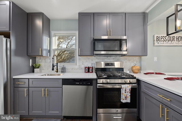 kitchen featuring appliances with stainless steel finishes, light countertops, a sink, and decorative backsplash