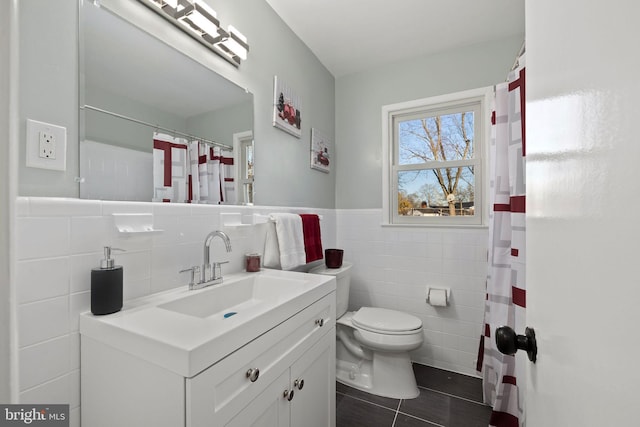 bathroom with wainscoting, toilet, tile patterned flooring, vanity, and tile walls