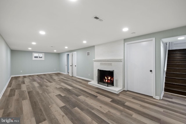 unfurnished living room with wood finished floors, a brick fireplace, visible vents, and stairs