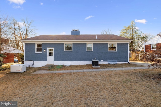 rear view of house featuring entry steps, central AC unit, a lawn, a chimney, and brick siding