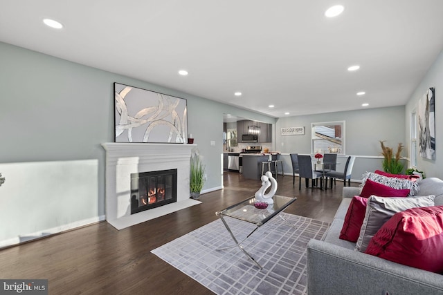 living area featuring a fireplace with flush hearth, baseboards, dark wood finished floors, and recessed lighting