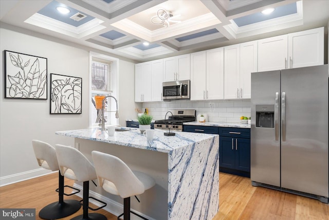 kitchen featuring stainless steel appliances, a sink, blue cabinetry, light wood-type flooring, and tasteful backsplash