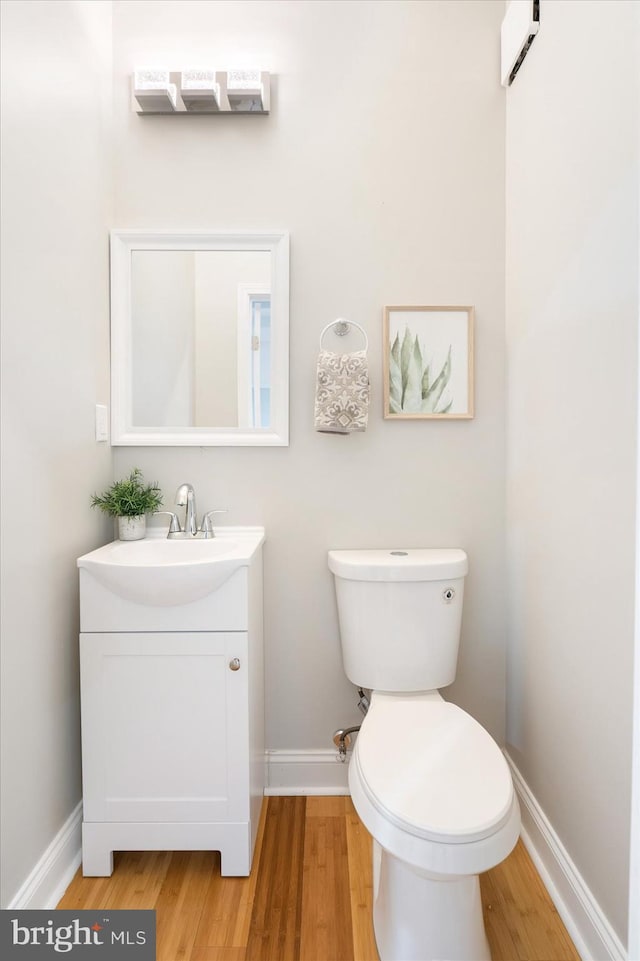 half bathroom featuring toilet, baseboards, wood finished floors, and vanity