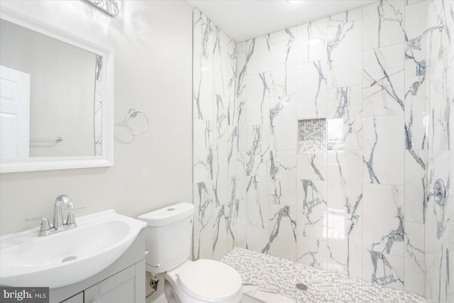 bathroom with toilet, a tile shower, and vanity