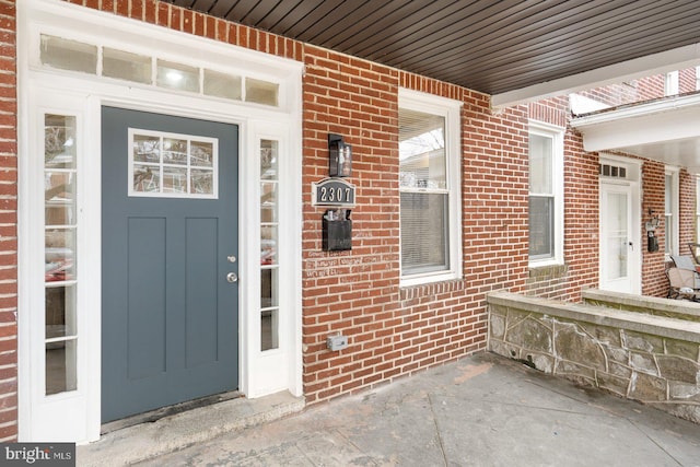 view of exterior entry with a porch and brick siding