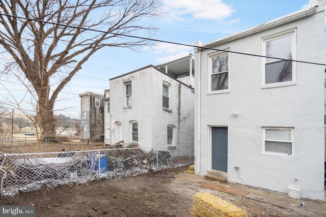 rear view of house with entry steps, fence, and stucco siding