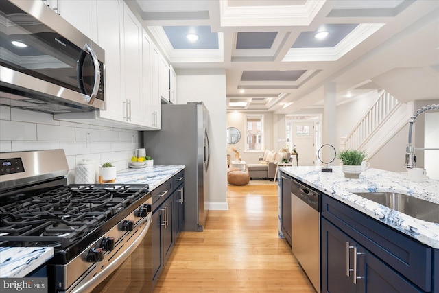 kitchen featuring coffered ceiling, white cabinets, light wood-style flooring, appliances with stainless steel finishes, and a sink