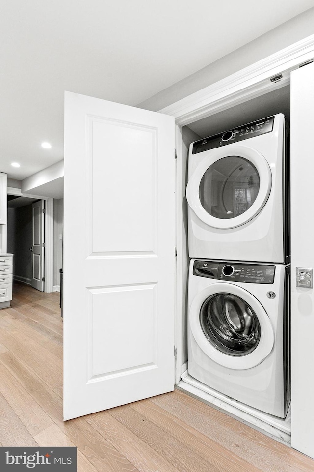 clothes washing area with laundry area, light wood-type flooring, stacked washing maching and dryer, and recessed lighting