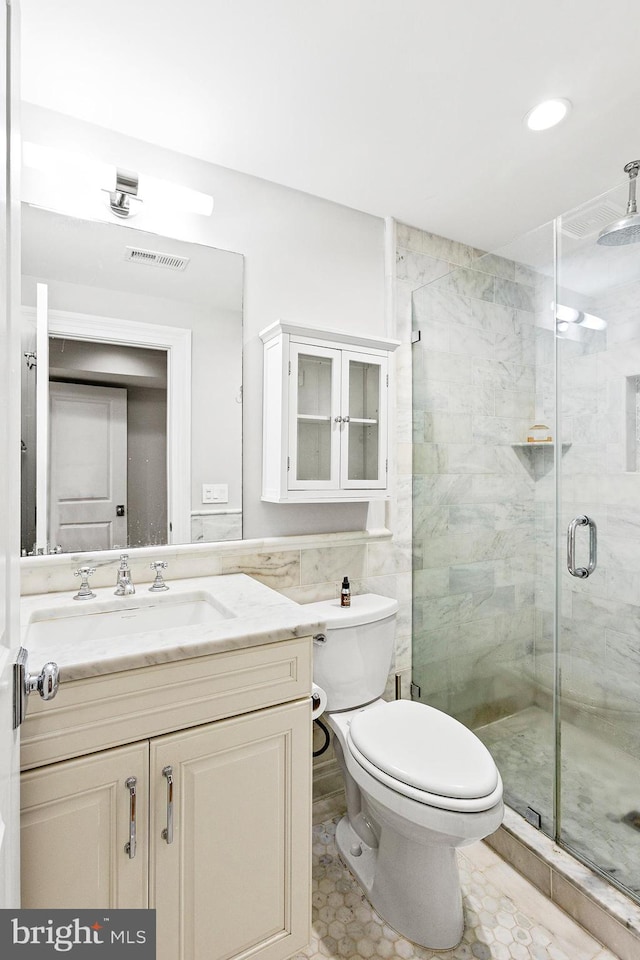 full bathroom with tile walls, visible vents, toilet, a shower stall, and vanity