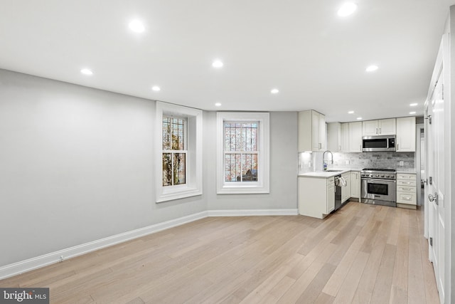 kitchen featuring stainless steel appliances, light countertops, backsplash, a sink, and light wood-type flooring