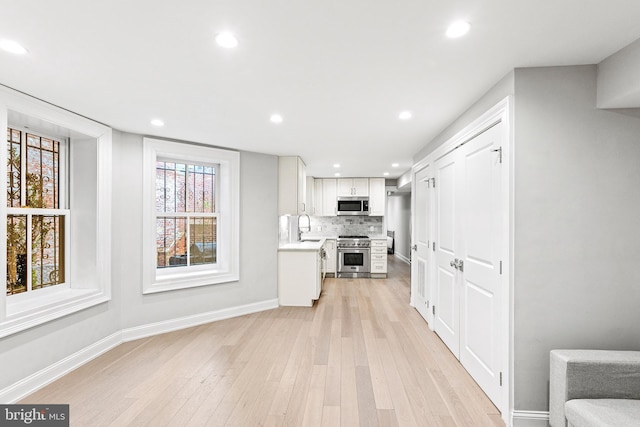 kitchen with stainless steel appliances, a sink, light countertops, light wood-type flooring, and decorative backsplash