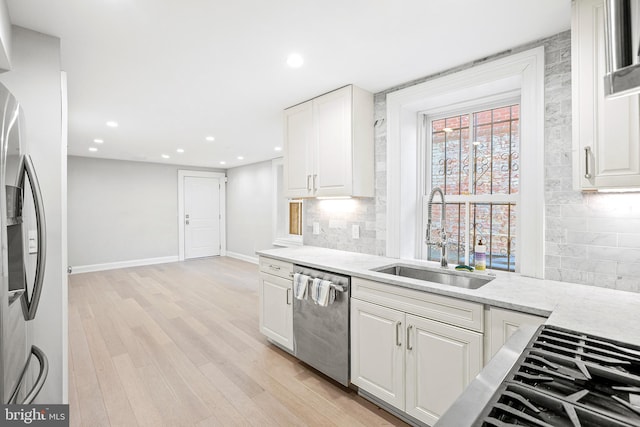 kitchen featuring stainless steel appliances, light wood-style flooring, a sink, and white cabinetry