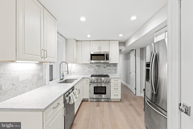 kitchen featuring stainless steel appliances, a sink, white cabinetry, light wood-style floors, and light countertops