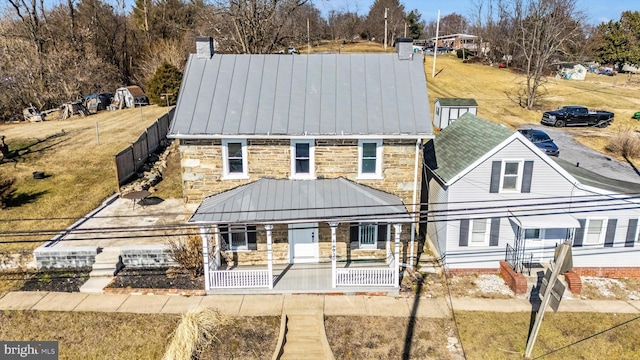 rear view of property featuring stone siding, covered porch, metal roof, and a chimney