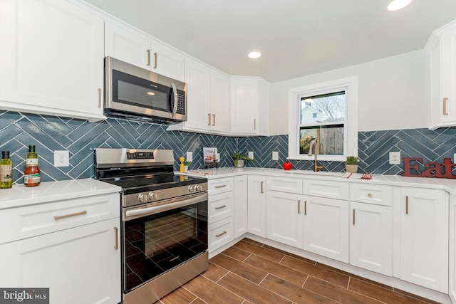 kitchen featuring decorative backsplash, wood tiled floor, stainless steel appliances, white cabinetry, and a sink