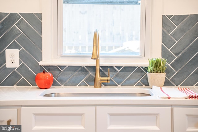 room details with white cabinets, backsplash, light countertops, and a sink