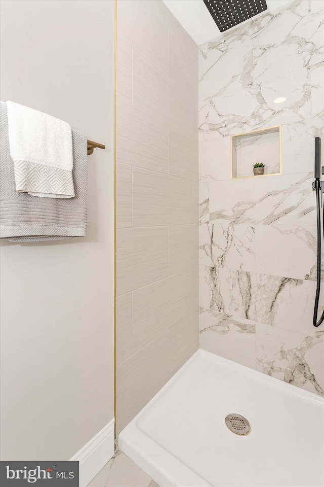 bathroom featuring marble finish floor, tiled shower, and baseboards