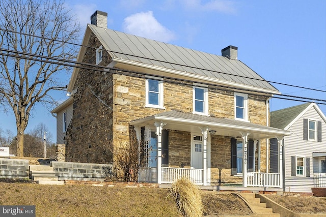 view of front of home featuring metal roof, a porch, stone siding, a standing seam roof, and a chimney