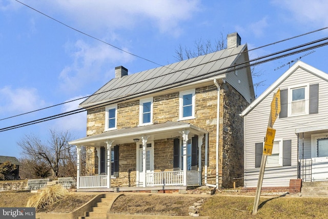 view of front facade featuring metal roof, a standing seam roof, stone siding, and covered porch