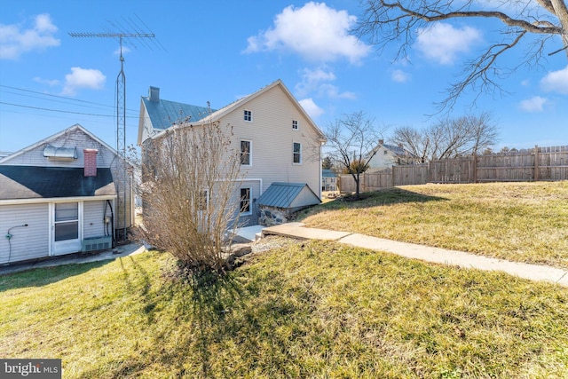 view of side of home with fence, a chimney, and a lawn