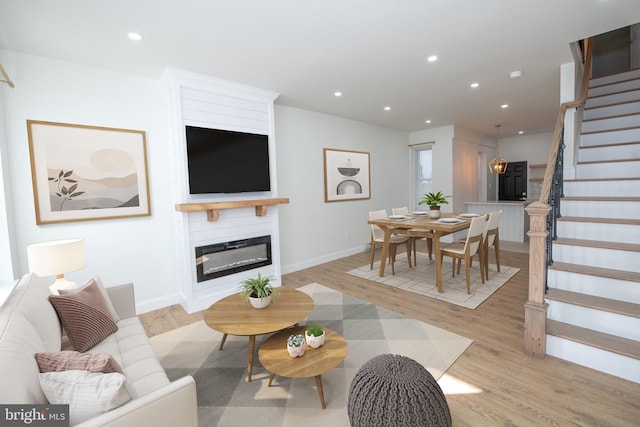 living room with recessed lighting, light wood-style flooring, a glass covered fireplace, baseboards, and stairs