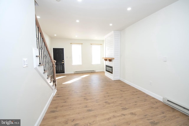 unfurnished living room featuring light wood-style floors, a fireplace, stairway, and baseboard heating