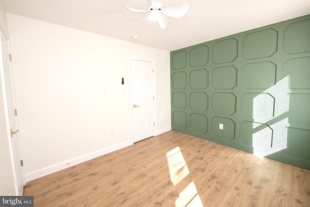 unfurnished bedroom with an accent wall, light wood finished floors, a ceiling fan, and baseboards