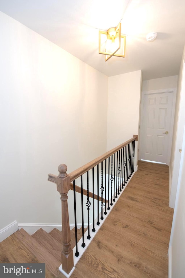 hall with wood finished floors, an upstairs landing, and baseboards