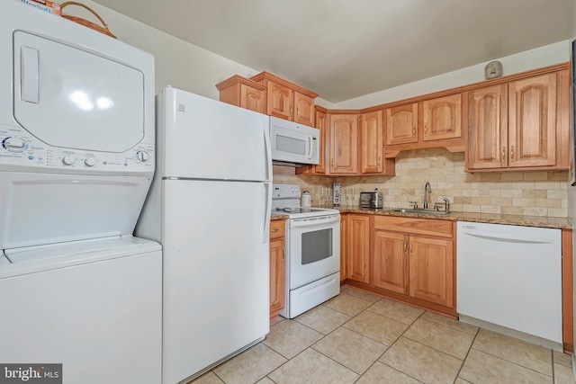 kitchen featuring white appliances, tasteful backsplash, light stone counters, stacked washer / drying machine, and a sink