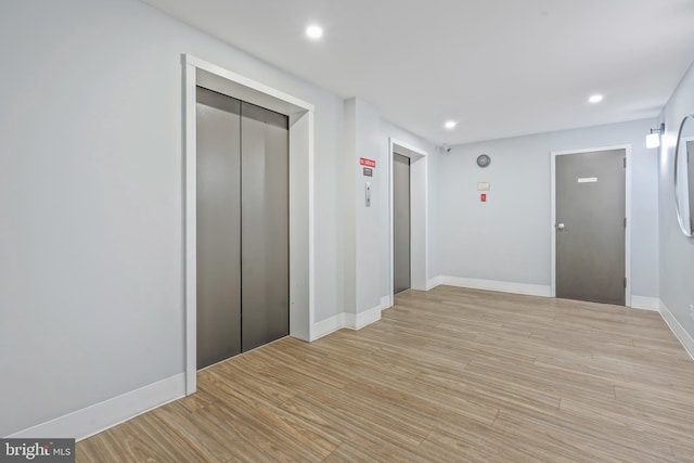 corridor with light wood-type flooring, elevator, baseboards, and recessed lighting