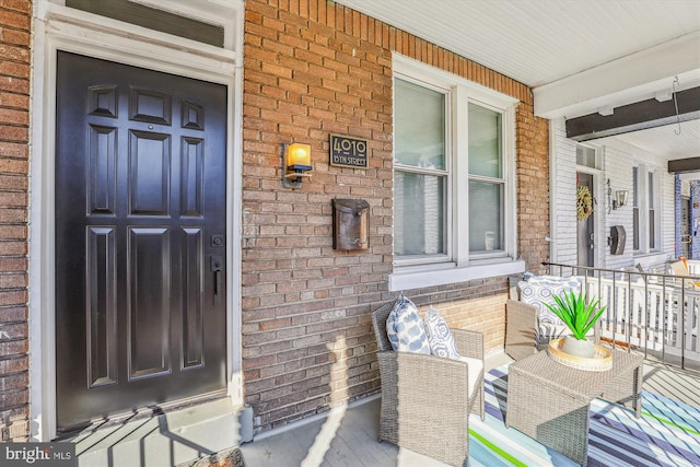 view of exterior entry with a porch and brick siding