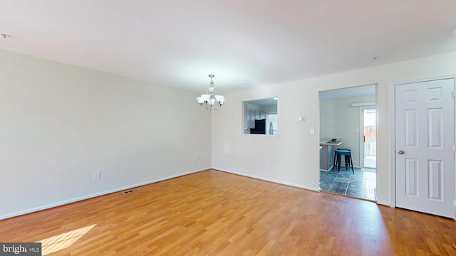 unfurnished room with an inviting chandelier, visible vents, baseboards, and wood finished floors