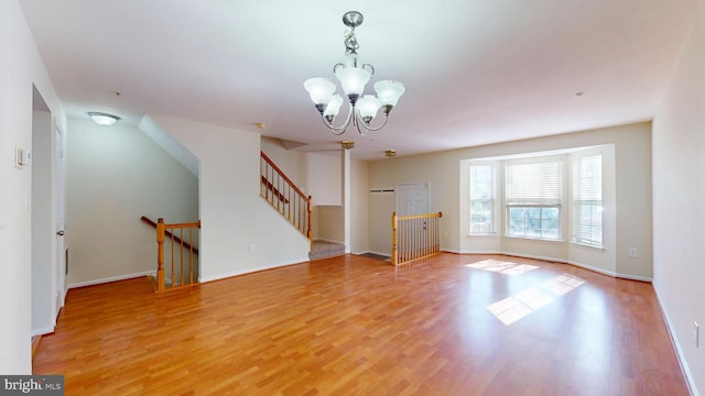 unfurnished living room with baseboards, stairway, an inviting chandelier, and wood finished floors