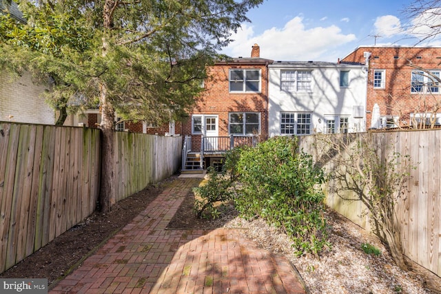 rear view of property with brick siding, a chimney, a fenced backyard, and a wooden deck