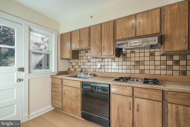 kitchen with under cabinet range hood, black dishwasher, light countertops, light wood finished floors, and stainless steel gas stovetop