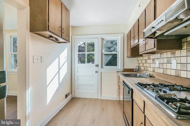 kitchen with tasteful backsplash, visible vents, light wood-style flooring, a sink, and under cabinet range hood