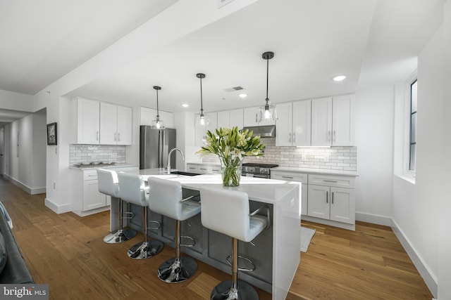 kitchen featuring light countertops, appliances with stainless steel finishes, a center island with sink, and white cabinetry