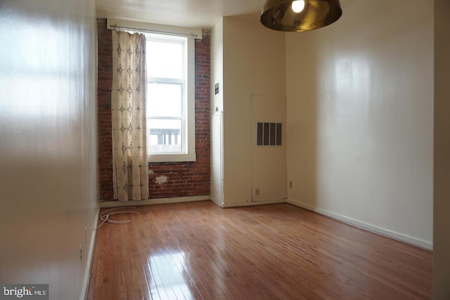 empty room featuring baseboards, light wood finished floors, and brick wall