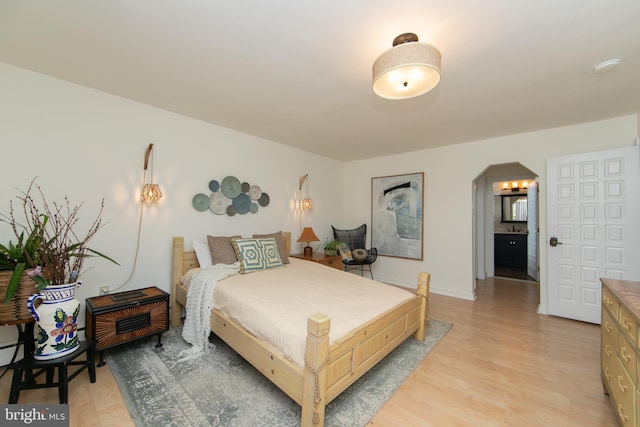 bedroom featuring light wood-style floors, baseboards, and arched walkways