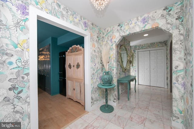 hall with a notable chandelier, marble finish floor, and wallpapered walls