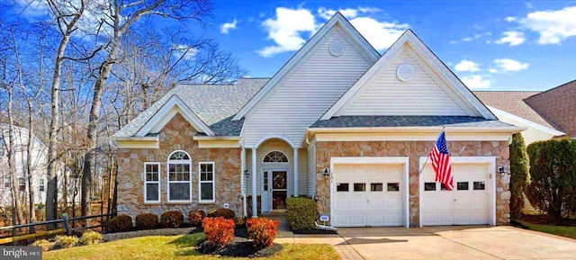 view of front of property featuring a garage, stone siding, a shingled roof, and driveway