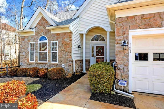 view of exterior entry featuring stone siding, roof with shingles, and an attached garage