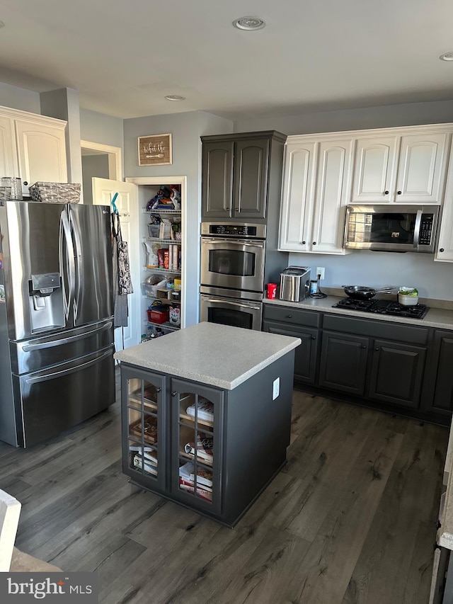 kitchen featuring gray cabinetry, stainless steel appliances, light countertops, dark wood finished floors, and glass insert cabinets