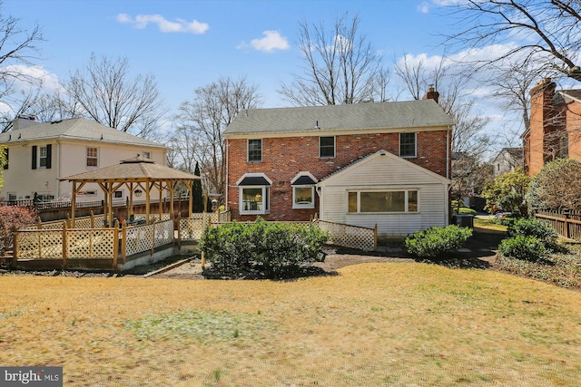 back of house featuring a lawn, fence, a gazebo, brick siding, and a chimney