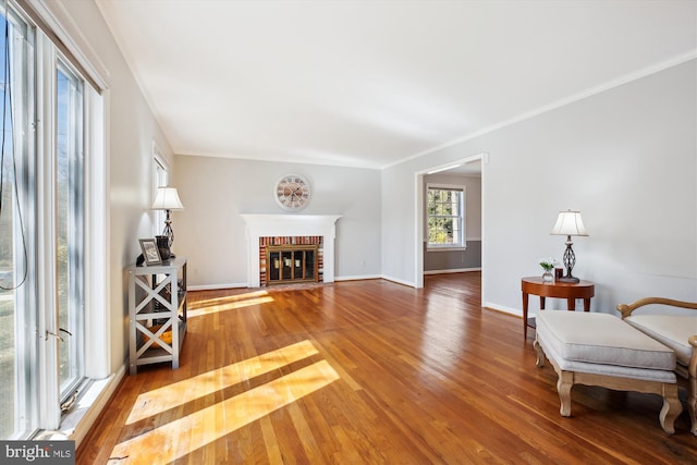 living area with hardwood / wood-style floors, crown molding, a brick fireplace, and baseboards