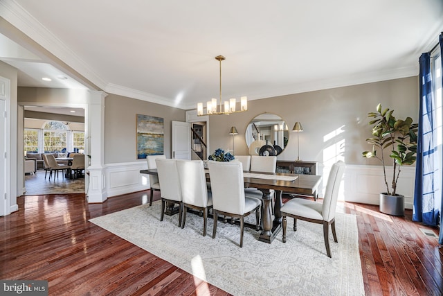 dining space featuring a chandelier, a wainscoted wall, dark wood-style flooring, decorative columns, and crown molding