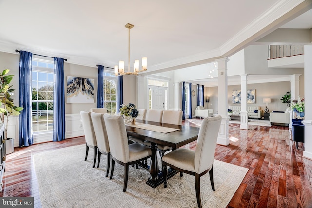 dining room with decorative columns, a wainscoted wall, wood-type flooring, ornamental molding, and an inviting chandelier