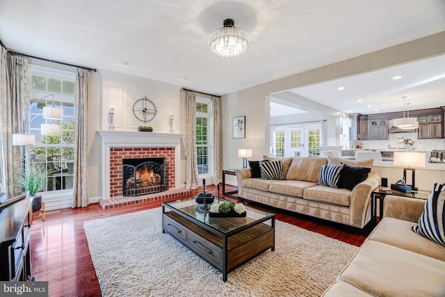 living room with a chandelier, recessed lighting, wood finished floors, baseboards, and a brick fireplace