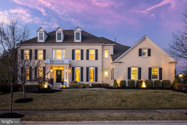 colonial home featuring a balcony, a lawn, and brick siding