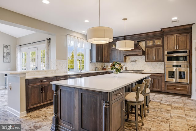 kitchen with a kitchen breakfast bar, custom exhaust hood, stainless steel appliances, light countertops, and backsplash